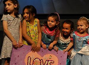A group of children on the church stage, with a big poster in front of them that says “LOVE”