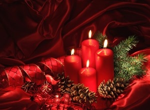 Red candles on Christmas fabric, surrounded by pine cones and some sprigs of a spruce tree